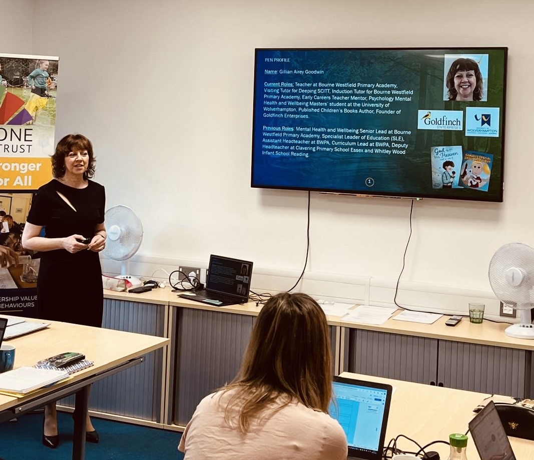 Gillian standing at the front of a classroom talking to course members with a large screen on the wall displaying course information